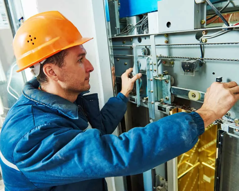 Técnico ajustando el tablero de control de un elevador durante una revisión de mantenimiento