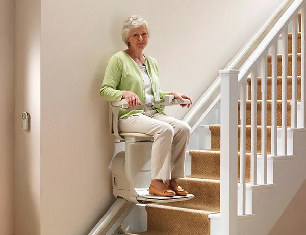 Persona adulta mayor subiendo una escalera de casa en una silla salvaescaleras